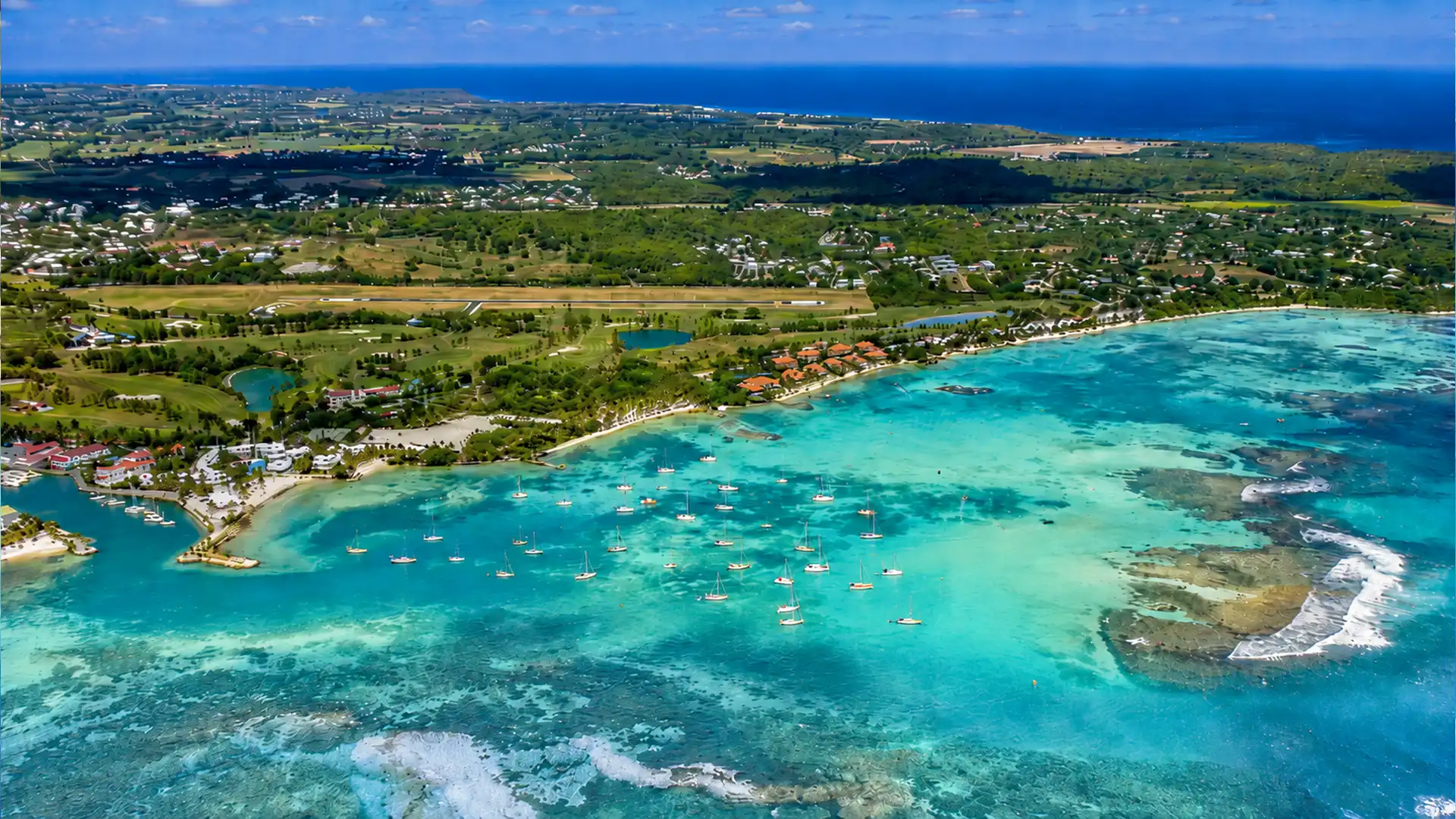 Vue aérienne du lagon de Saint-François en Guadeloupe, avec voiliers, plages, récifs coralliens et golf en arrière-plan.